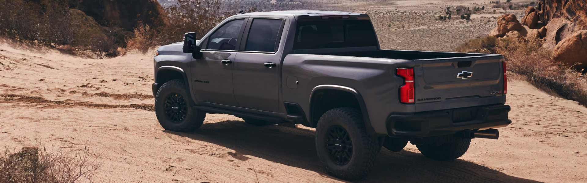 2025 Chevrolet Silverado 1500 driving off-road on a sandy desert trail, showcasing its rugged performance and capability.